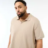 Remera polo de manga corta color beige, con cuello camisero sin botones y textura sutil de rayas verticales en relieve. Corte regular y diseño holgado.