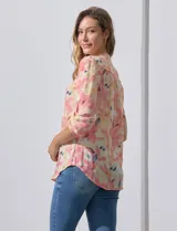 Blusa de gasa estampada con flores en tonos rosa, amarillo y azul. Tiene cuello a la base, escote en V y botones. La delantera tiene detalle plisado y las mangas son 3/4 regulables con presilla y botón.