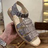 Sandalia de cuero color gris topo con textura de cocodrilo. Diseño cerrado en la parte delantera con tiras entrecruzadas y abertura en la punta. Posee tira ajustable con hebilla metálica en el tobillo.