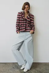 Blazer Zara Woman Collection de corte entallado con bajo peplum, confeccionada en tejido de mezcla de algodón con estampado de cuadros en tonos rojo, azul marino y blanco. Presenta cuello solapa, manga larga, bolsillos delanteros y cierre frontal con botones metálicos en relieve.