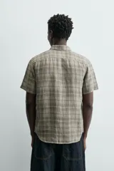 Camisa de lino color beige de corte relajado, con cuello solapa, manga corta y cierre frontal con botones.