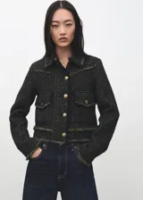 Chaqueta corta confeccionada en tejido texturizado con mezcla de algodón, poliéster y lana. Presenta cuello solapa, mangas largas, bolsillos frontales con solapa y cierre mediante botones metálicos dorados. Los bordes cuentan con detalles de flecos deshilachados.