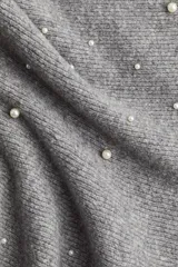 Top strapless de tejido de punto gris, ajustado al cuerpo con peplum acampanado en la parte inferior. Está adornado con perlas y pequeños cristales distribuidos por toda la prenda.