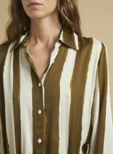 Vestido camisero largo con rayas verticales color marrón y blanco, de corte recto y manga larga. Tiene cuello camisero, cierre frontal con botones y cordón ajustable en la cintura.