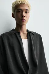 Camisa de corte relajado confeccionada en tejido fluido con mezcla de viscosa y lyocell. Presenta cuello polo, manga larga con puños abotonados y un diseño cruzado con cierre frontal de botones.