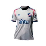 Camiseta de fútbol Umbro del Club Nacional de Football, modelo Home 2025 para mujer. Diseño blanco con detalles en azul y rojo en el cuello, hombros y mangas. Incluye el logo de Umbro, el escudo del club y sponsors impresos.