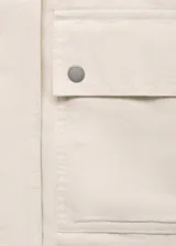 Chaqueta recta de algodón estilo vaquero, color blanco, con manga larga, cuello camisero de efecto piel en contraste, cierre oculto de cremallera y botones, y dos bolsillos delanteros de parche con solapa.