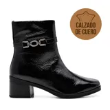 Bota corta de cuero negro charol con punta cuadrada y cierre lateral. Tiene una tira con hebilla metálica plateada alrededor del tobillo y taco cuadrado bajo.