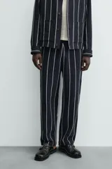 Pantalón de corte relajado, color azul marino, con rayas verticales blancas finas. Presenta cintura elástica ajustable con cordón interior y bolsillos laterales y traseros de plastrón.