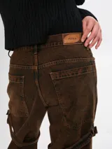 Pantalón de jean marrón con efecto gastado, corte ancho, bolsillos cargo y correas con hebillas a la altura de los muslos.