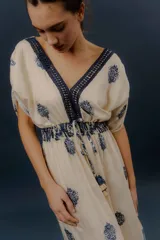 Vestido largo beige con estampado paisley en color azul marino, escote en V profundo con detalle bordado, mangas cortas amplias, cordón ajustable en la cintura con borlas y volados en el ruedo.