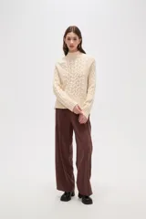 Polera de tejido de punto color crema, con cuello alto y diseño de trenzas verticales. Presenta mangas largas con puños acanalados y un corte holgado.