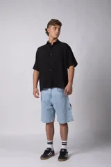 Camisa de manga corta de color verde militar, confeccionada en una mezcla de lino y viscosa. Posee un calce regular, cuello plano y cierre frontal con botones, destacándose por su textura liviana y respirable.