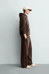 Pantalón jogger de corte relajado y pernera ancha, confeccionado en tejido de algodón con interior perchado. Presenta cintura elástica con cordón interior, bolsillos laterales y un bolsillo trasero de plastrón.