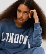 Buzo cerrado de fleece color azul, con cuello redondo, mangas largas, puños y ruedo ajustados. Presenta estampa frontal con la palabra "LONDON" en letras blancas con borde oscuro.