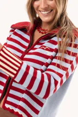 Saco tejido de punto a rayas horizontales en color celeste y rojo, con cuello alto, cierre frontal doble deslizador y puños con diseño en contraste. Presenta un pequeño bordado en el pecho.