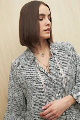 Camisa de calce relajado con estampado lineal irregular en blanco y negro. Presenta cuello clásico, abotonadura frontal, mangas largas con puños camiseros y detalles de recortes verticales en el frente.