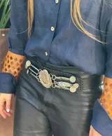 Cinturón tipo rastra color beige con apliques metálicos plateados y escudo de Uruguay en el centro.