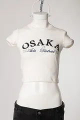 Remera baby tee de morley color chocolate, de calce ajustado al cuerpo y manga corta, con cuello redondo y diseño estampado frontal.