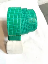 Cinto verde esmeralda con textura de cocodrilo y hebilla rectangular de hueso.