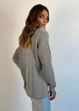 Buzo de tejido de punto ligero, color dorado con brillo sutil, escote en V y manga larga con diseño calado en los puños.