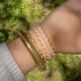 Pulsera tejida a mano con cuentas Miyuki en tonos beige y dorado, con diseño de flecos que aporta textura y movimiento.