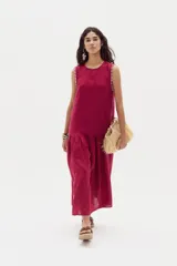 Vestido midi de lino color beige, sin mangas, con cuello redondo y detalles de ondas en las sisas. Presenta un corte con volante fruncido en la parte inferior.