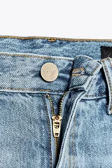 Pantalón de jean celeste de tiro alto, corte recto y largo hasta el tobillo. Tiene cinco bolsillos, trabillas en la cintura, efecto lavado y cierre frontal con cremallera y botón.