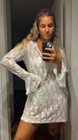 Vestido corto de encaje blanco con botones frontales y mangas largas acampanadas.