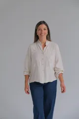 Blusa de lino color beige con cuello mao y detalles de volados sutiles. Presenta bordados florales en color blanco en el frente y mangas largas con puños elásticos.