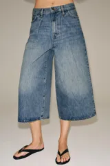 Bermuda de denim de tiro medio y corte wide leg, con diseño culotte, trabillas en la cintura y pliegues delanteros. Posee cinco bolsillos y cierre frontal con cremallera y botón.