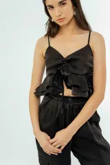 Musculosa negra de satén con breteles finos, escote en V, volados en el ruedo y lazo ajustable en el frente.