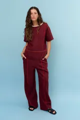 Pantalon de lino color marrón con costuras blancas decorativas a lo largo de las piernas y corte amplio.