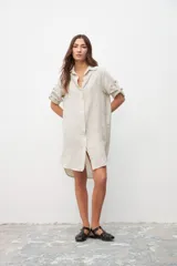 Vestido tipo camisa color crudo, de corte recto, con cuello camisero, mangas 3/4 con trabillas y cierre frontal con botones.