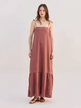 Vestido largo de algodón denim con diseño de rayas verticales en color azul marino y beige. Cuenta con tirantes finos ajustables con lazos en los hombros, escote recto y corte suelto con un volante en el bajo.