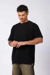 Remera de corte oversized en color marrón, confeccionada en tejido de algodón con textura de micropanal. Presenta cuello redondo con detalle de costura en forma de X y mangas cortas de estilo caído.