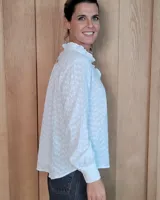 Blusa de manga larga con estampado de rayas verticales finas en tono beige. Presenta cuello redondo con volados, cierre frontal parcial con botones y puños con volados.