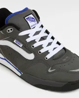 Zapatillas Vans Rowley XLT de color gris oscuro, con la franja lateral Sidestripe en blanco, pasador de cordones con etiqueta de la marca y detalles en azul. Presentan diseño robusto inspirado en el skate de los años 90 y 2000, con lengüeta acolchada y suela combinada en blanco y negro.