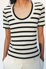 Camiseta de manga corta confeccionada en tejido de algodón con textura rib. Presenta un diseño a rayas horizontales en color blanco y negro, con un escote redondo pronunciado y bajo recto.