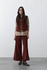 Chaleco de pana color marrón oscuro, con cuello camisero, cierre frontal de botones metálicos dorados y dos bolsillos frontales con detalle de bordado geométrico.