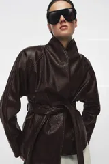 Chaqueta de Zara Woman Collection confeccionada en tejido efecto piel con textura granulada. Presenta cuello solapa, manga larga y cierre frontal con cinturón ajustable anudado a la cintura. Incluye forro interior.