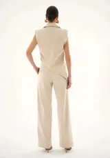 Chaleco sastrero color beige con diseño asimétrico en el bajo, escote en V, botones forrados y hombreras que aportan estructura.