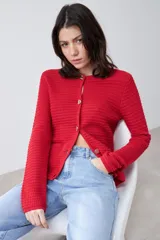 Chaqueta de punto color rojo, de corte entallado y manga larga. Presenta cuello redondo y cierre frontal con botones metálicos dorados texturizados.