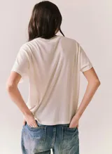 Remera blanca de manga corta y cuello redondo, con estampado frontal de estilo retro con la inscripción "Just a Small Town Girl Journey" acompañada de gráficos florales en tonos rojo, amarillo y azul.