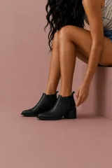 Botinetas de cuero negro con punta fina, taco cuadrado de madera de 6 cm y paneles laterales elásticos con tachas decorativas.