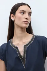 Remera blanca de algodón con escote en V y detalles de bordado étnico en tonos rojizos y naranjas en el cuello y los hombros. De corte recto y manga corta.