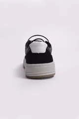 Zapatillas urbanas de cuero negro con detalles en cuero gamuzado y cuero perforado. Presentan una banda lateral blanca y suela de goma color tiza.