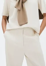 Pantalón de lino color beige, de corte recto y tiro medio, con detalle de pequeña abertura y botón en el dobladillo inferior.