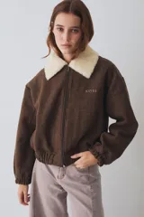 Campera bomber marrón de paño de lana, con cierre frontal, cuello de corderito sintético blanco desmontable, bolsillos laterales, puños y dobladillo elásticos, y logo bordado en el pecho.