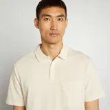 Remera tipo polo color crema, de piqué de algodón, con cuello clásico, tapeta de dos botones y bolsillo de parche en el pecho.